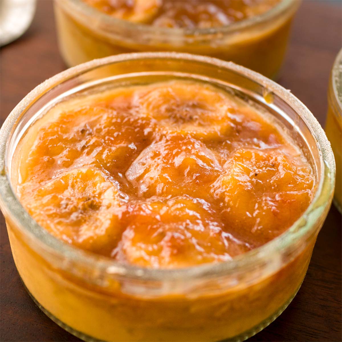 Close-up of banana foster pudding in a glass bowl, topped with warm caramelized banana sauce and glossy banana slices.