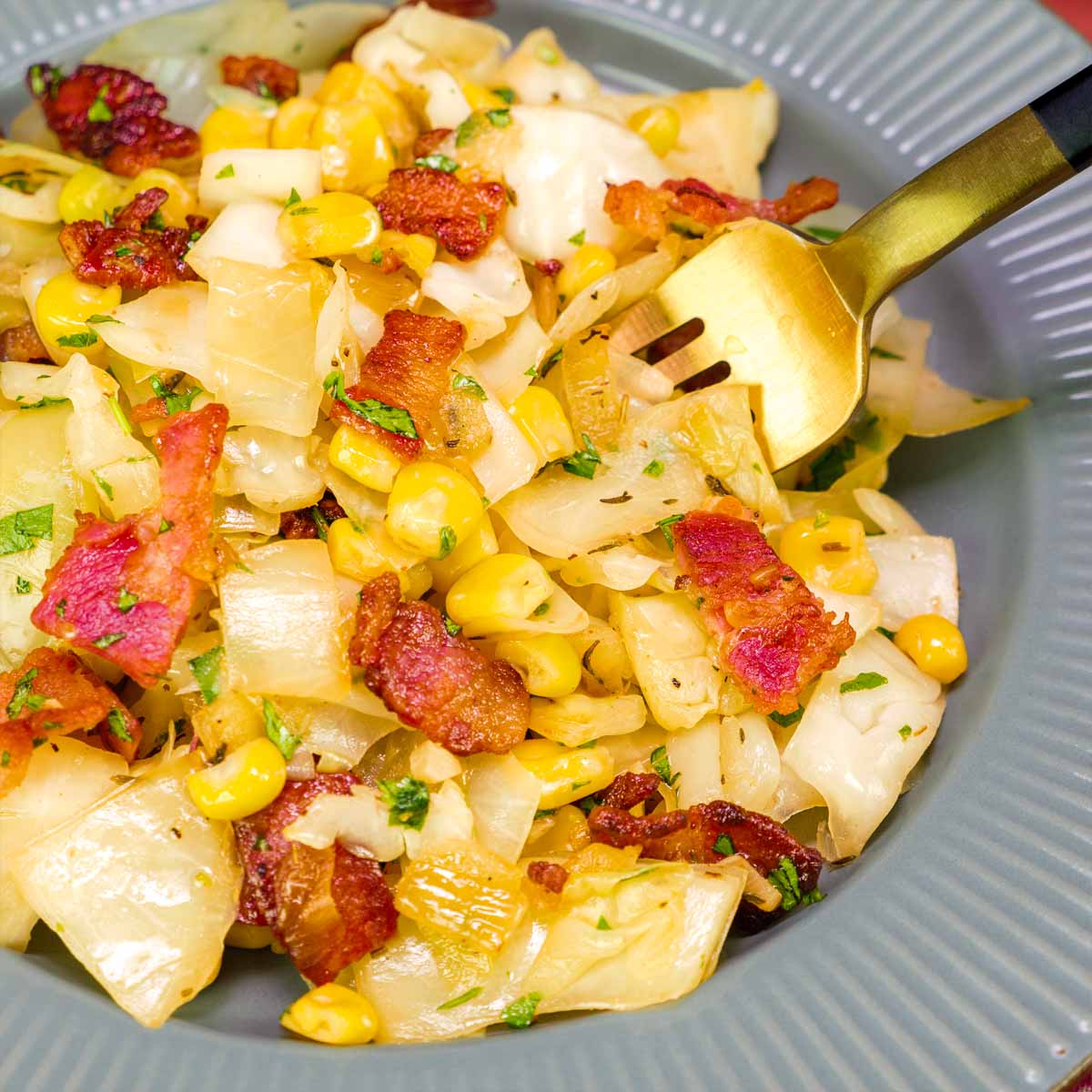 Close-up of fried cabbage with sweet corn and crispy bacon, served on a gray plate with a fork. 