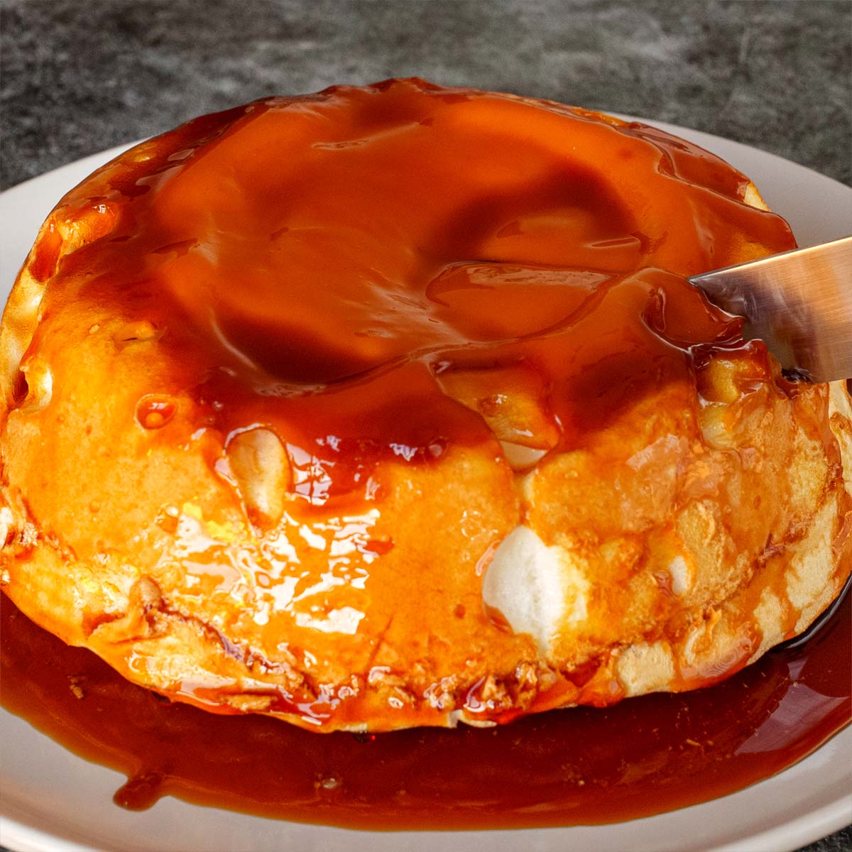 Molotof Cake (Portuguese meringue cake) covered in glossy caramel sauce, being sliced on a plate.