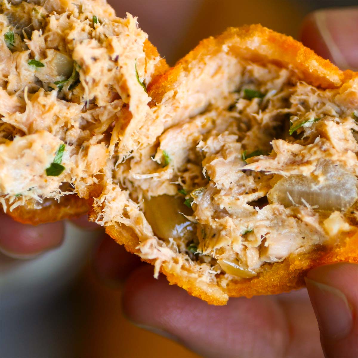 Close-up of a tuna croquette broken open, showing its creamy tuna filling with herbs and vegetables inside a crispy golden coating. 