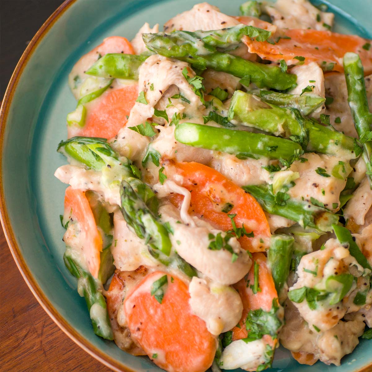 Easy Chicken and Asparagus Stir Fry with sliced carrots and a creamy garlic sauce, garnished with fresh parsley in a green plate.