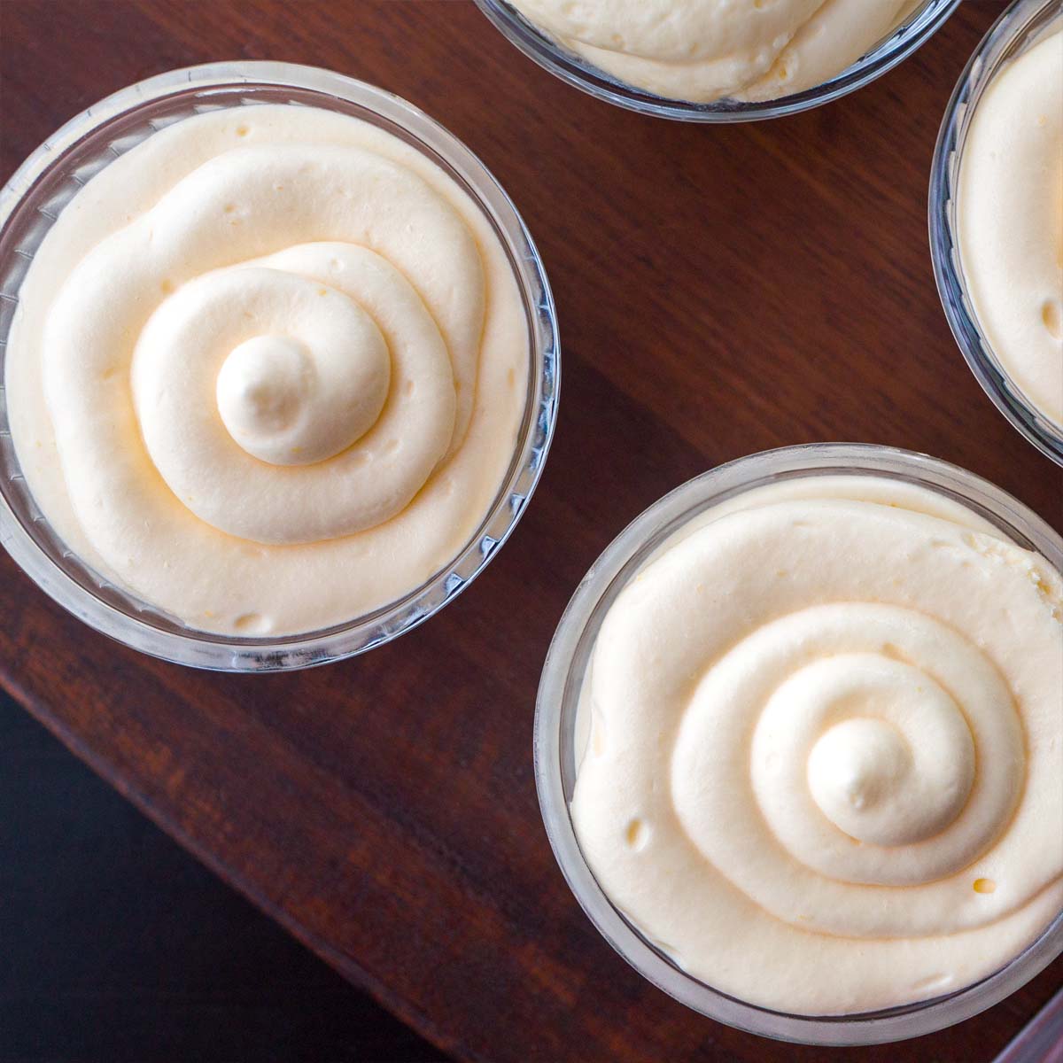 Top view of lemon curd mousse cups with smooth swirled tops on a wooden board
