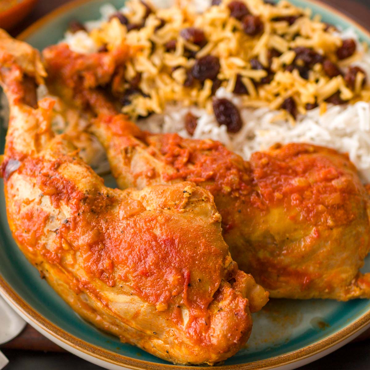 Close-up of Persian chicken simmered in saffron tomato sauce, served with saffron rice and sweet raisins in a bowl. 