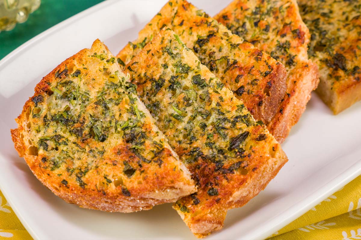 Golden crispy garlic sourdough toast slices with fresh parsley and herbs on a white serving plate.