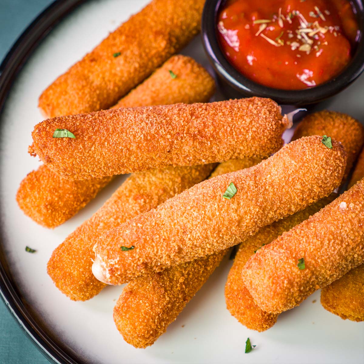 Close-up of crispy homemade mozzarella sticks on a plate, garnished with herbs and served with marinara sauce.