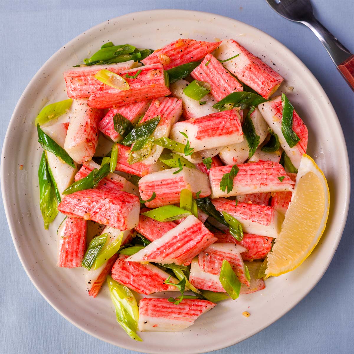 Sautéed imitation crabmeat tossed in garlic butter with sliced green onions and parsley, served in a bowl with a lemon wedge and cracked black pepper. 