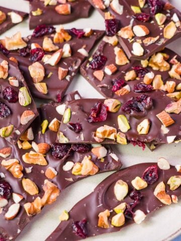 Close-up of dark chocolate bark shards on a plate, topped with chopped nuts, pistachios, and dried cranberries.