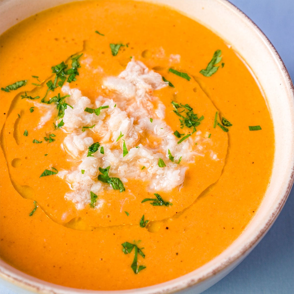 Close-up of creamy crab bisque garnished with lump crab meat and chopped parsley in a white bowl.