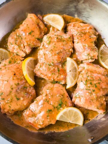 Lemon dill chicken thighs simmering in a creamy pan sauce with lemon wedges and fresh dill in a skillet