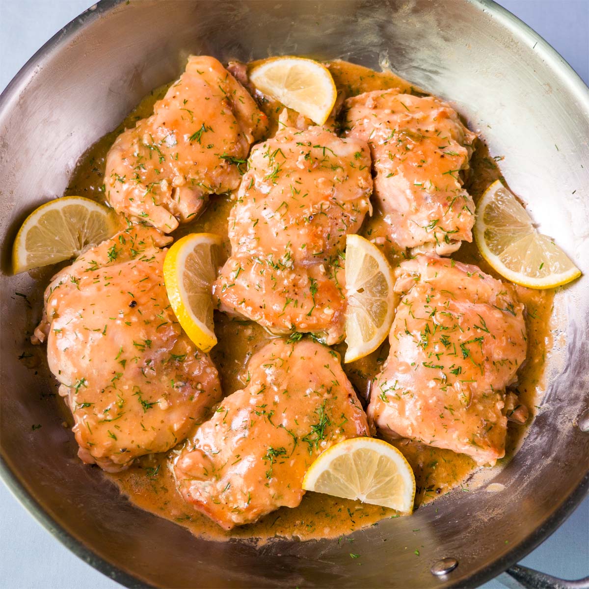 Lemon dill chicken thighs simmering in a creamy pan sauce with lemon wedges and fresh dill in a skillet