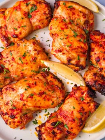 Baked harissa chicken thighs on a white plate with lemon wedges and a sprinkle of fresh parsley.