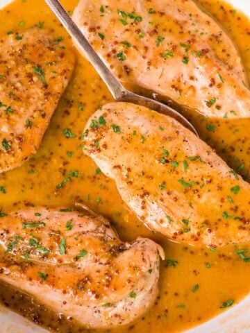 Creamy honey mustard chicken breasts simmering in a golden mustard sauce, finished with a sprinkle of parsley.