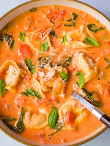 Creamy tomato tortellini soup with cheese tortellini, spinach, and fresh basil in a bowl with a spoon