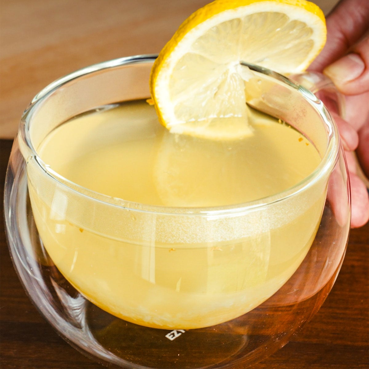 Lemon honey ginger tea in a clear glass cup with a lemon slice garnish.