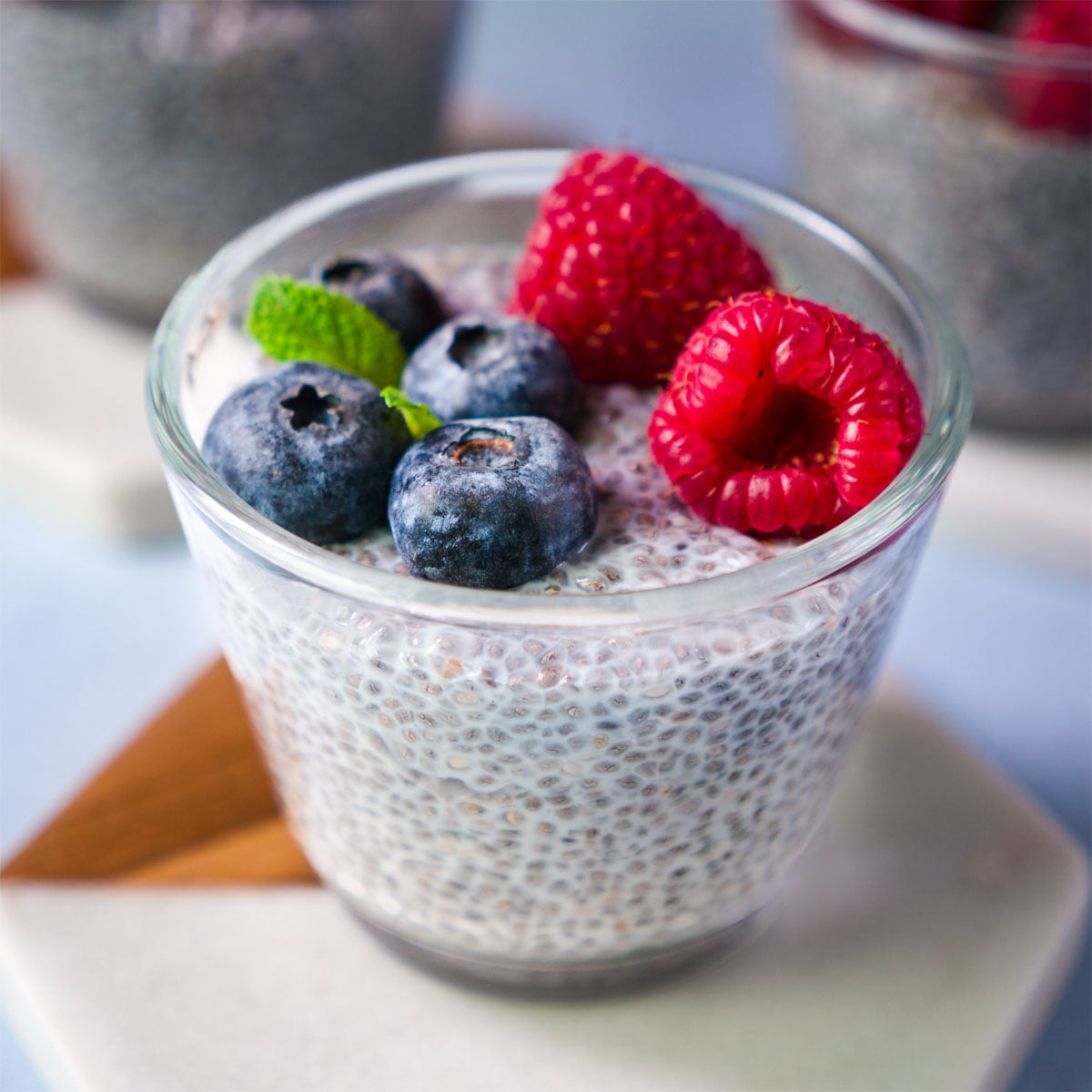 Overnight chia pudding in a glass topped with fresh blueberries, raspberries, and a mint leaf.