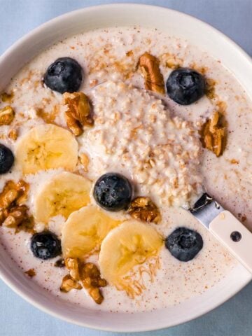 Creamy overnight oats with Greek yogurt topped with banana slices, blueberries, walnuts, and a spoon in the bowl.