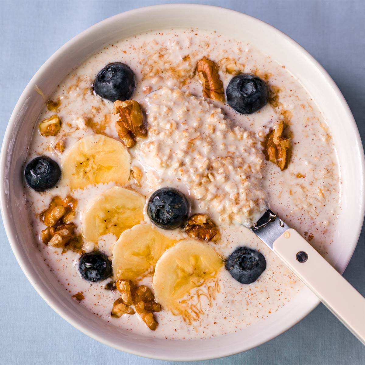 Creamy overnight oats with Greek yogurt topped with banana slices, blueberries, walnuts, and a spoon in the bowl.
