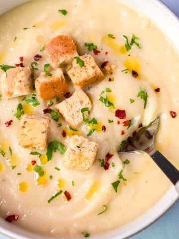 Creamy parsnip soup topped with croutons, chopped parsley, red pepper flakes, and a drizzle of olive oil, with a spoon in the bowl