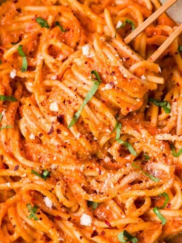 Creamy sweet potato pasta sauce tossed with spaghetti, topped with herbs and black pepper in a close-up pan