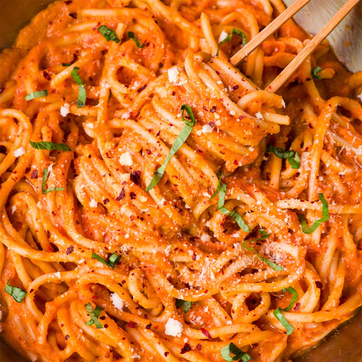 Creamy sweet potato pasta sauce tossed with spaghetti, topped with herbs and black pepper in a close-up pan