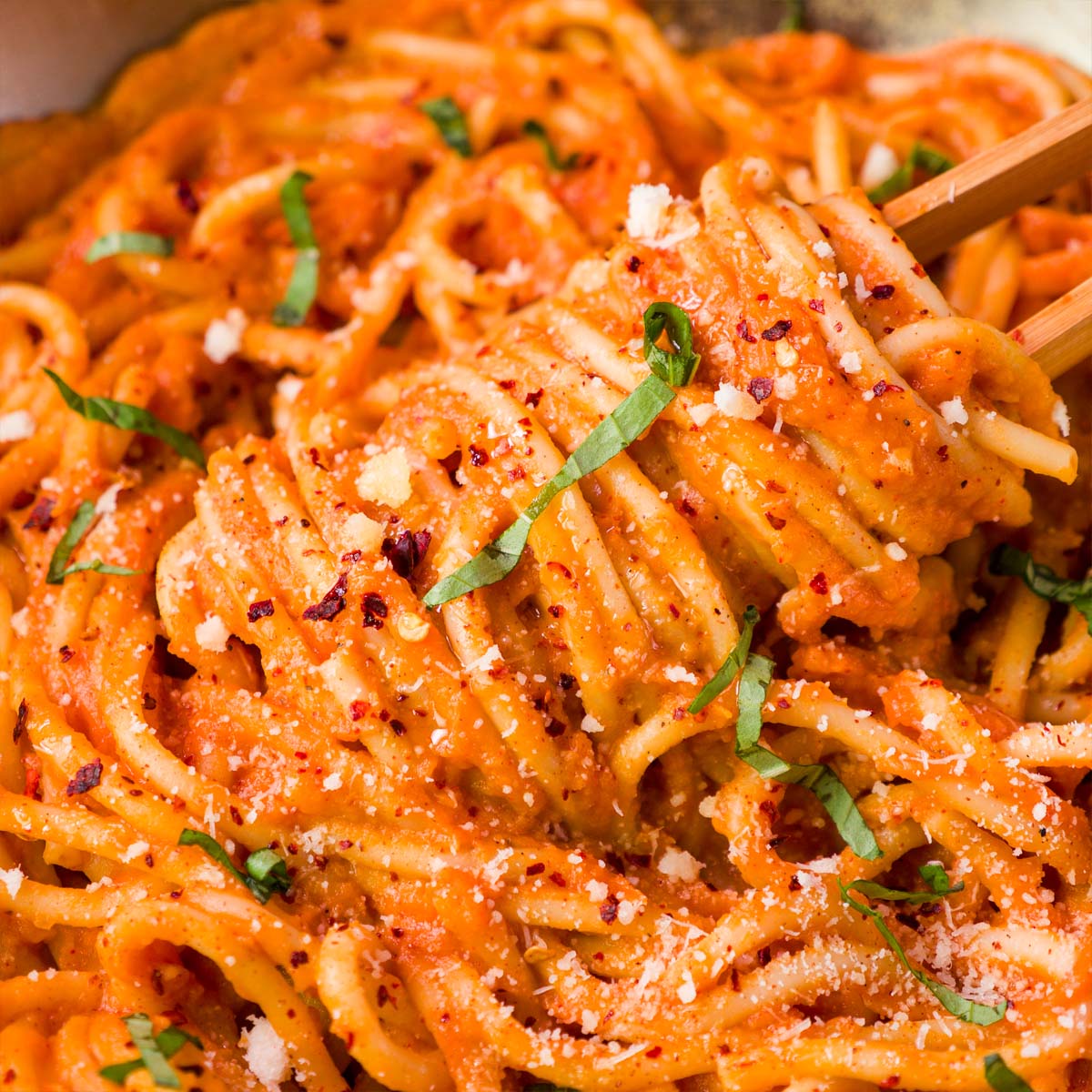 Close-up of spaghetti coated in creamy sweet potato pasta sauce with parmesan, basil, and red pepper flakes