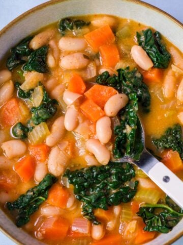 Close up of Creamy white bean and kale soup with carrots, tender white beans, and wilted kale served in a bowl with a spoon