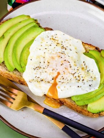 Avocado toast with runny over-easy egg on whole grain bread, seasoned with black pepper, served on ceramic plate