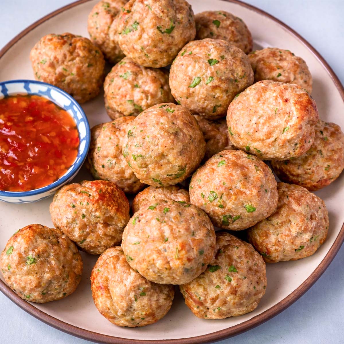 Golden baked chicken meatballs on a plate with sweet chili dipping sauce, close-up view