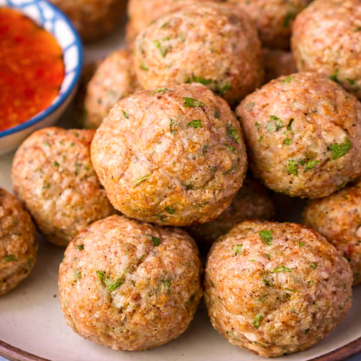 Close-up of golden baked chicken meatballs with parsley on a plate, served with sweet chili sauce