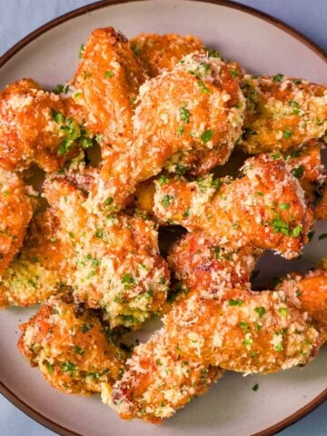 Crispy baked garlic parmesan chicken wings on a plate, coated in garlic butter with grated parmesan and chopped parsley.
