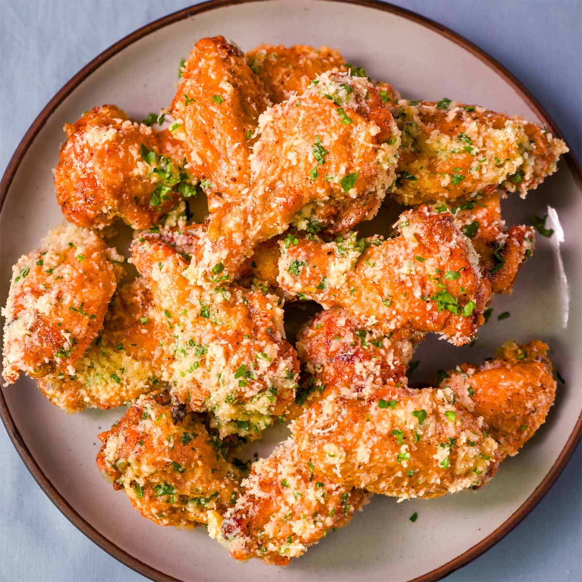 Crispy baked garlic parmesan chicken wings on a plate, coated in garlic butter with grated parmesan and chopped parsley.