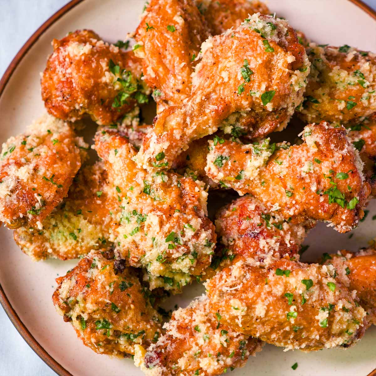 Close up Crispy baked garlic parmesan chicken wings on a plate, coated in garlic butter with grated parmesan and chopped parsley.