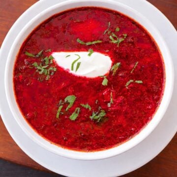 Overhead view of Ukrainian borscht beet soup in a white bowl, topped with sour cream and fresh herbs.