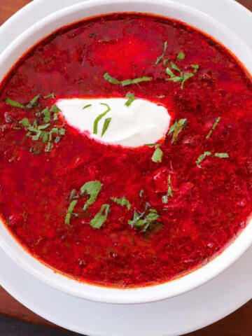 Overhead view of Ukrainian borscht beet soup in a white bowl, topped with sour cream and fresh herbs.