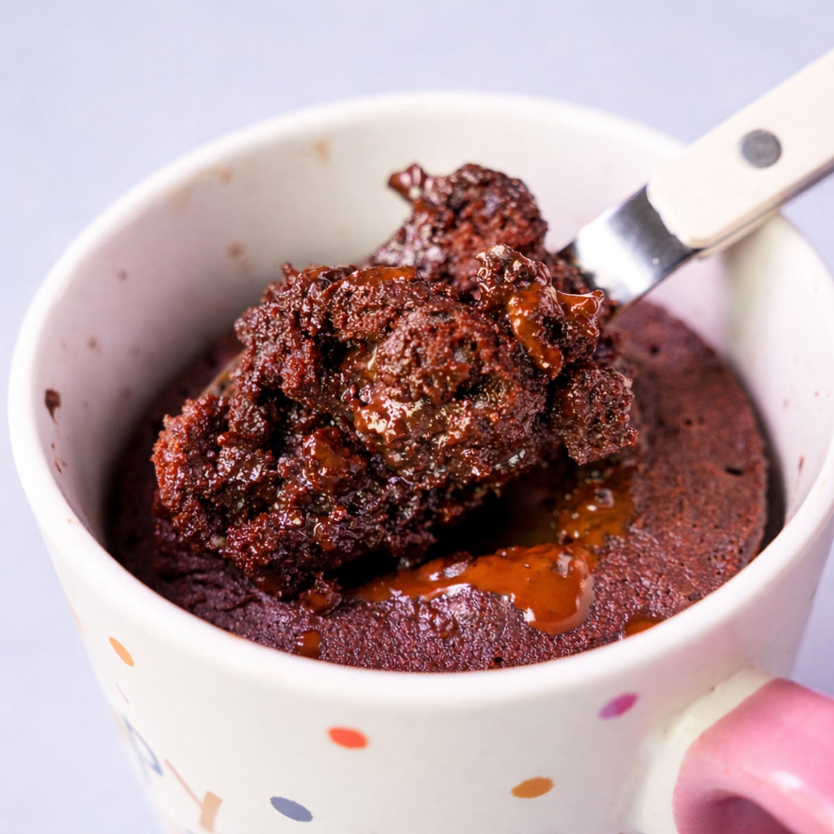 Spoonful of gooey chocolate lava mug cake lifted from a polka-dot mug, showing the molten chocolate center.