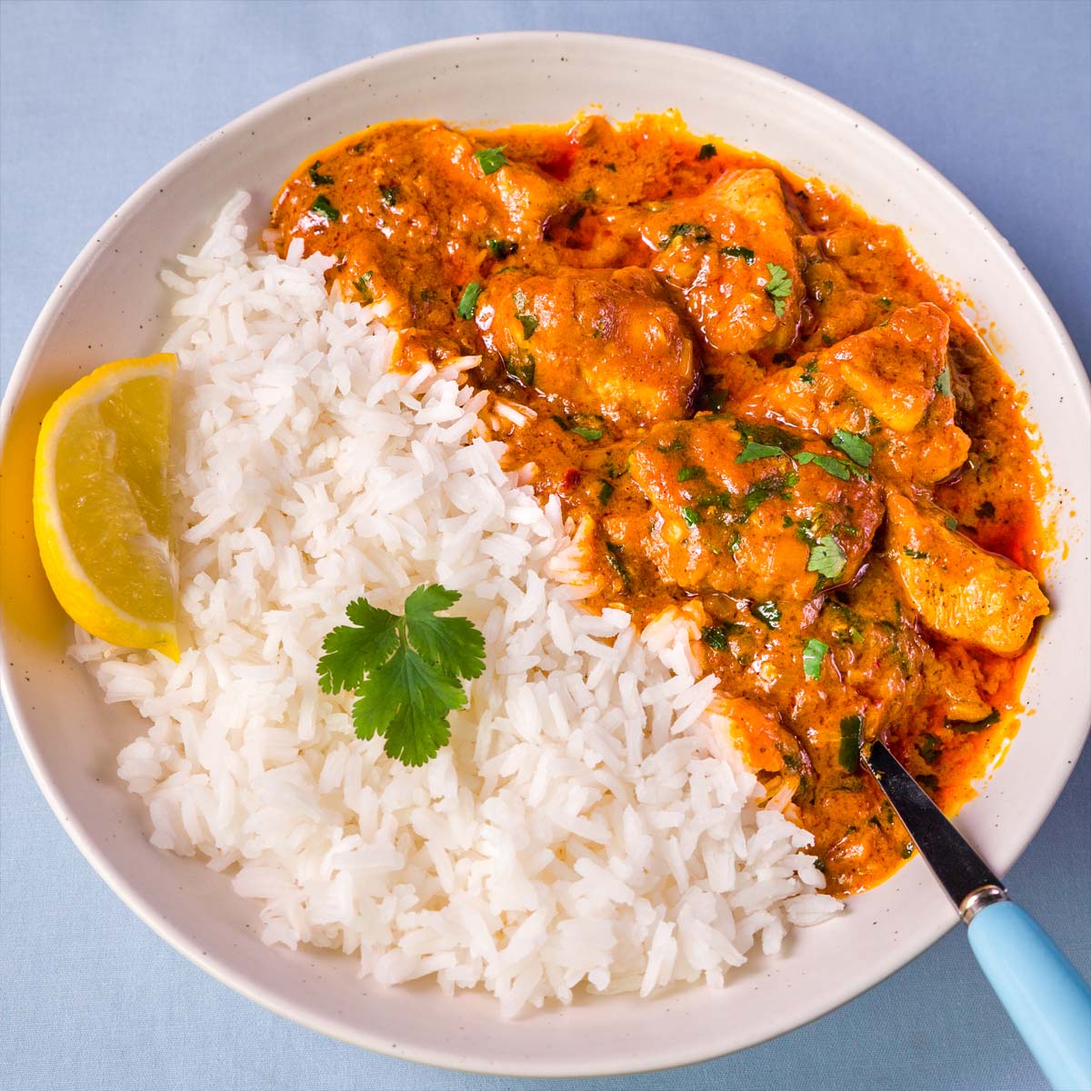 Creamy coconut chicken curry served with white rice, lemon wedge, and cilantro in a white bowl