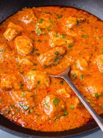 Creamy coconut chicken curry simmering in a black pan with a spoon, finished with chopped cilantro