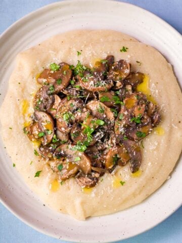 Creamy mushroom polenta topped with garlic white wine cremini mushrooms, parsley, and olive oil in a white bowl