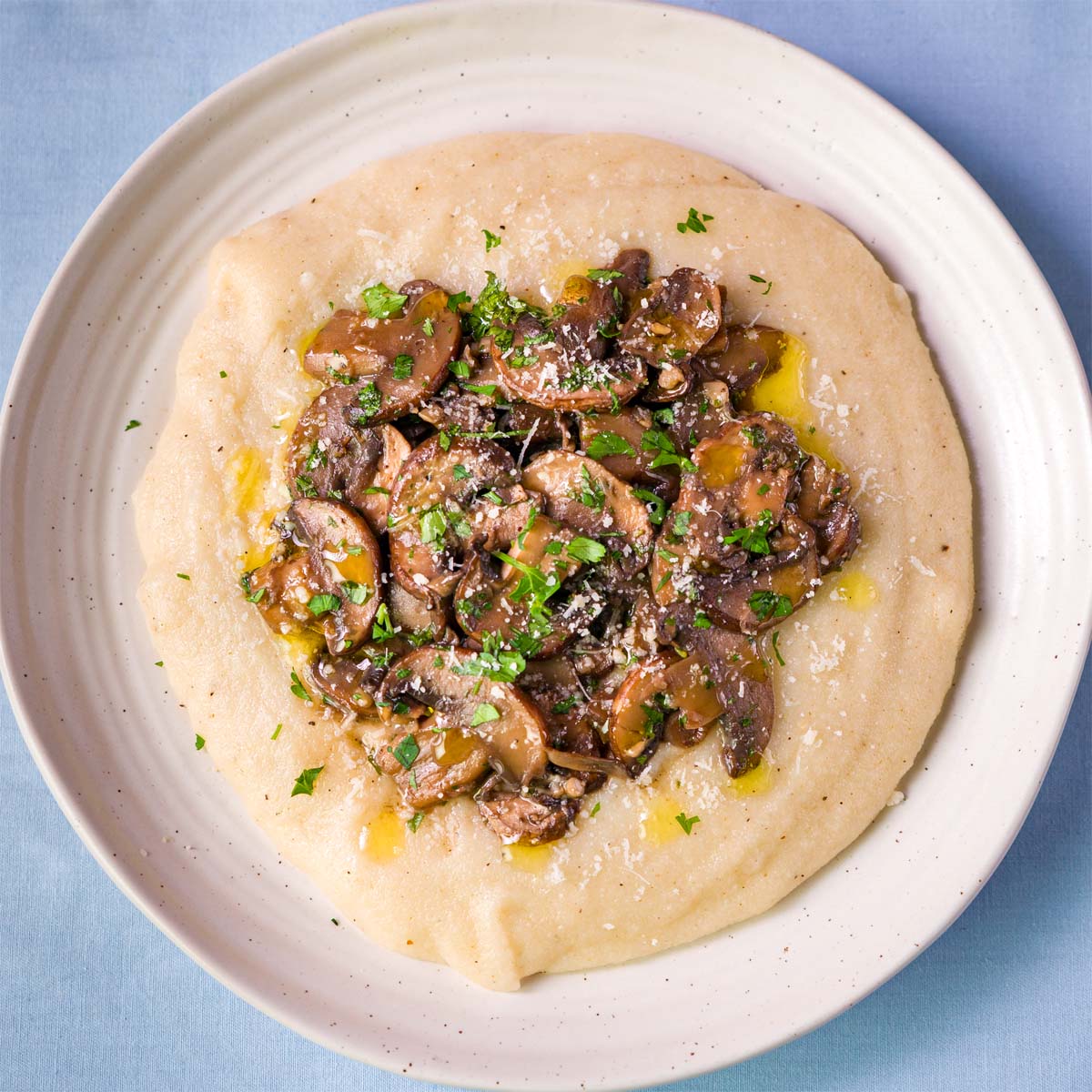 Creamy mushroom polenta topped with garlic white wine cremini mushrooms, parsley, and olive oil in a white bowl