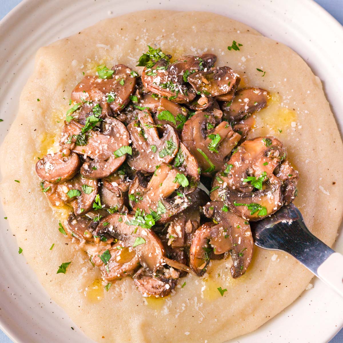 Creamy mushroom polenta with garlic white wine cremini mushrooms, parsley, and a spoon in the bowl
