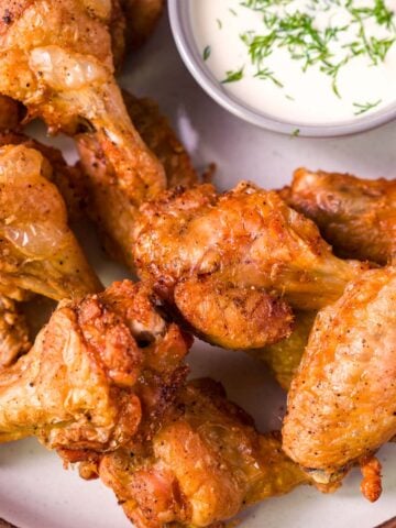 Crispy oven baked chicken wings on a plate with a bowl of creamy herb dipping sauce