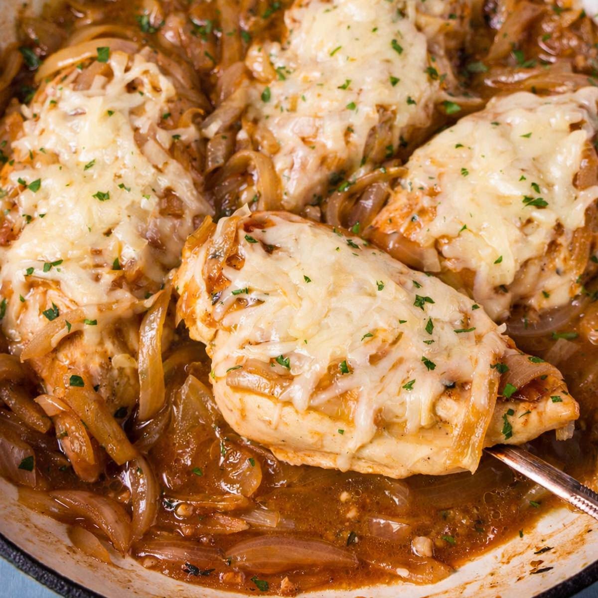 Close-up of French onion chicken skillet with cheesy chicken breast lifted over caramelized onion sauce