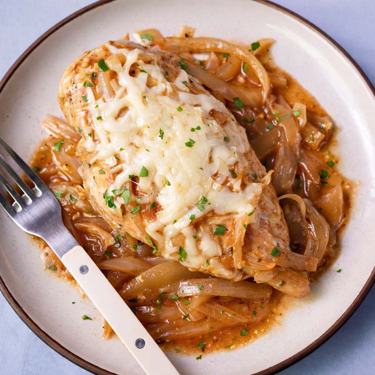 French onion chicken served on a plate with melted cheese and caramelized onions in rich pan sauce