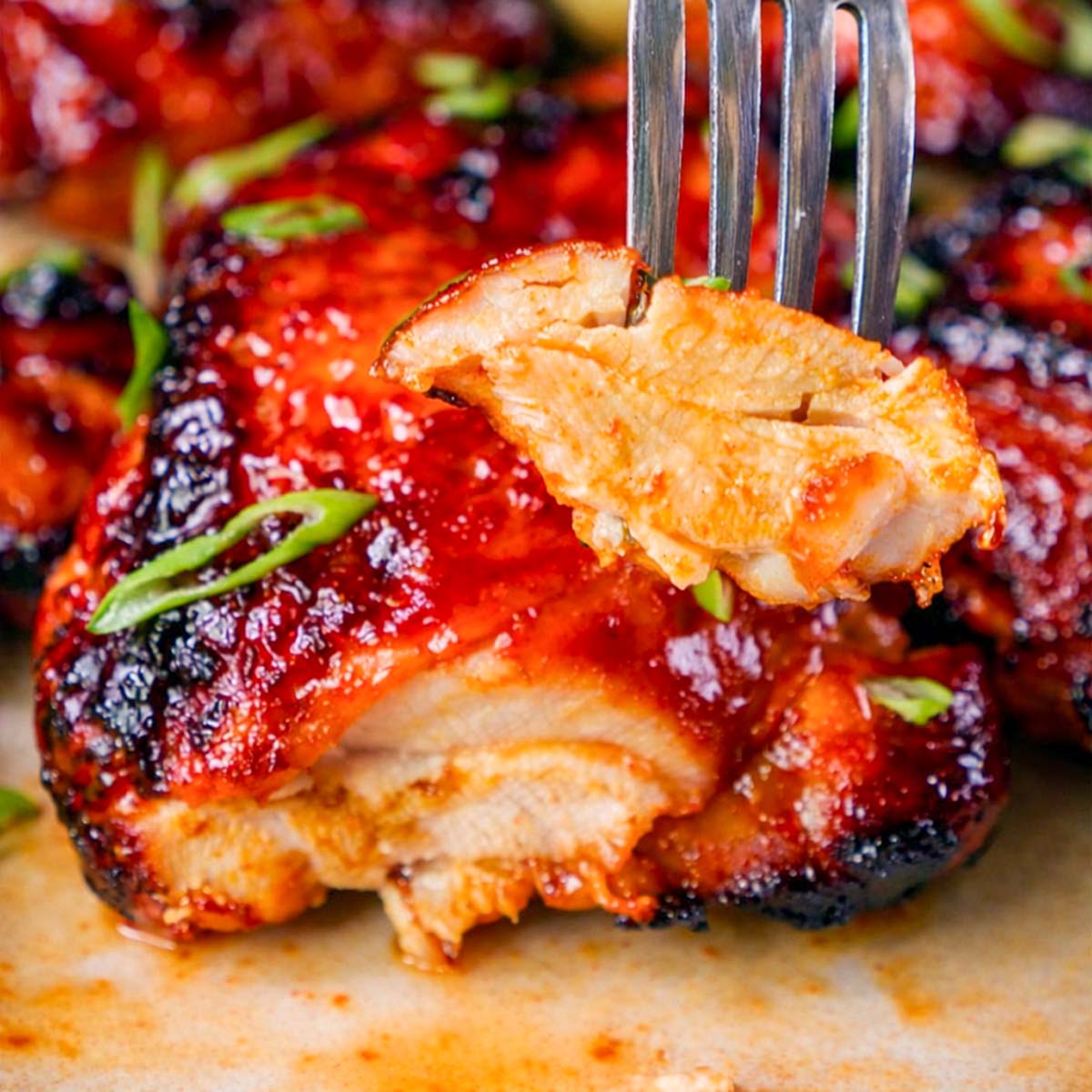 Fork lifting a juicy bite of gochujang-glazed chicken thigh with sliced green onions