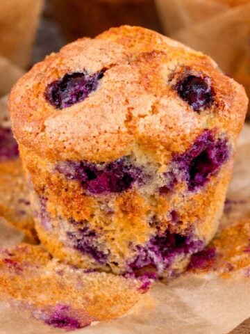 High-protein blueberry muffin with a golden top and juicy blueberries, wrapped in brown muffin paper.