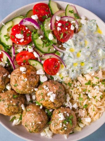 Mediterranean baked chicken meatball bowl with lemon rice, cucumber tomato salad, feta, and creamy tzatziki