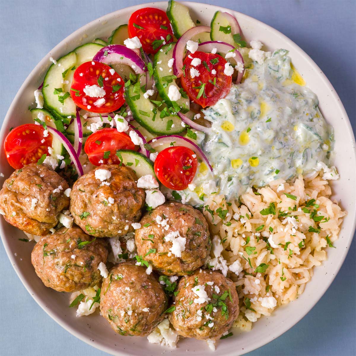 Mediterranean baked chicken meatball bowl with lemon rice, cucumber tomato salad, feta, and creamy tzatziki