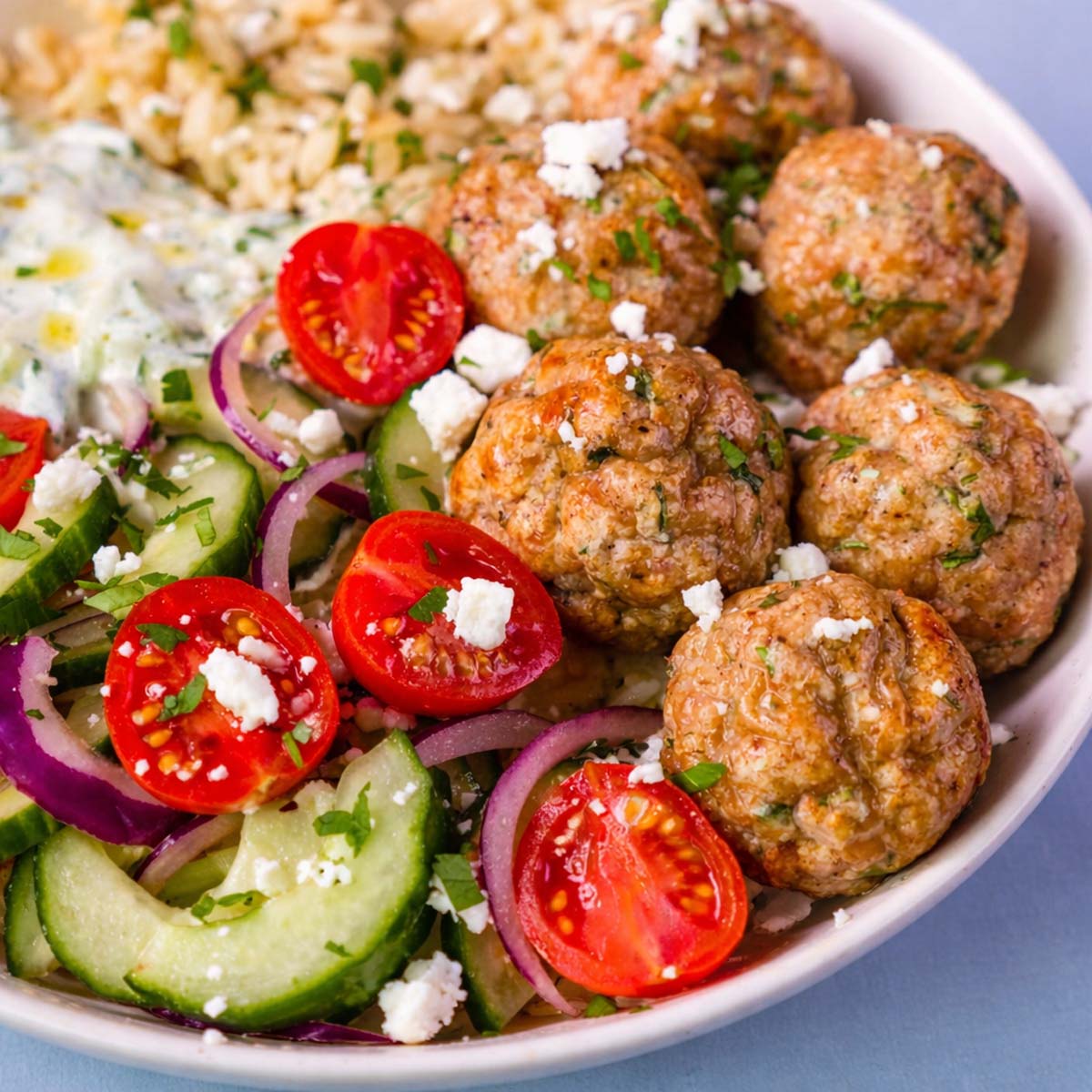 Close-up Mediterranean chicken meatball bowl with cucumber salad, cherry tomatoes, red onion, feta, and tzatziki