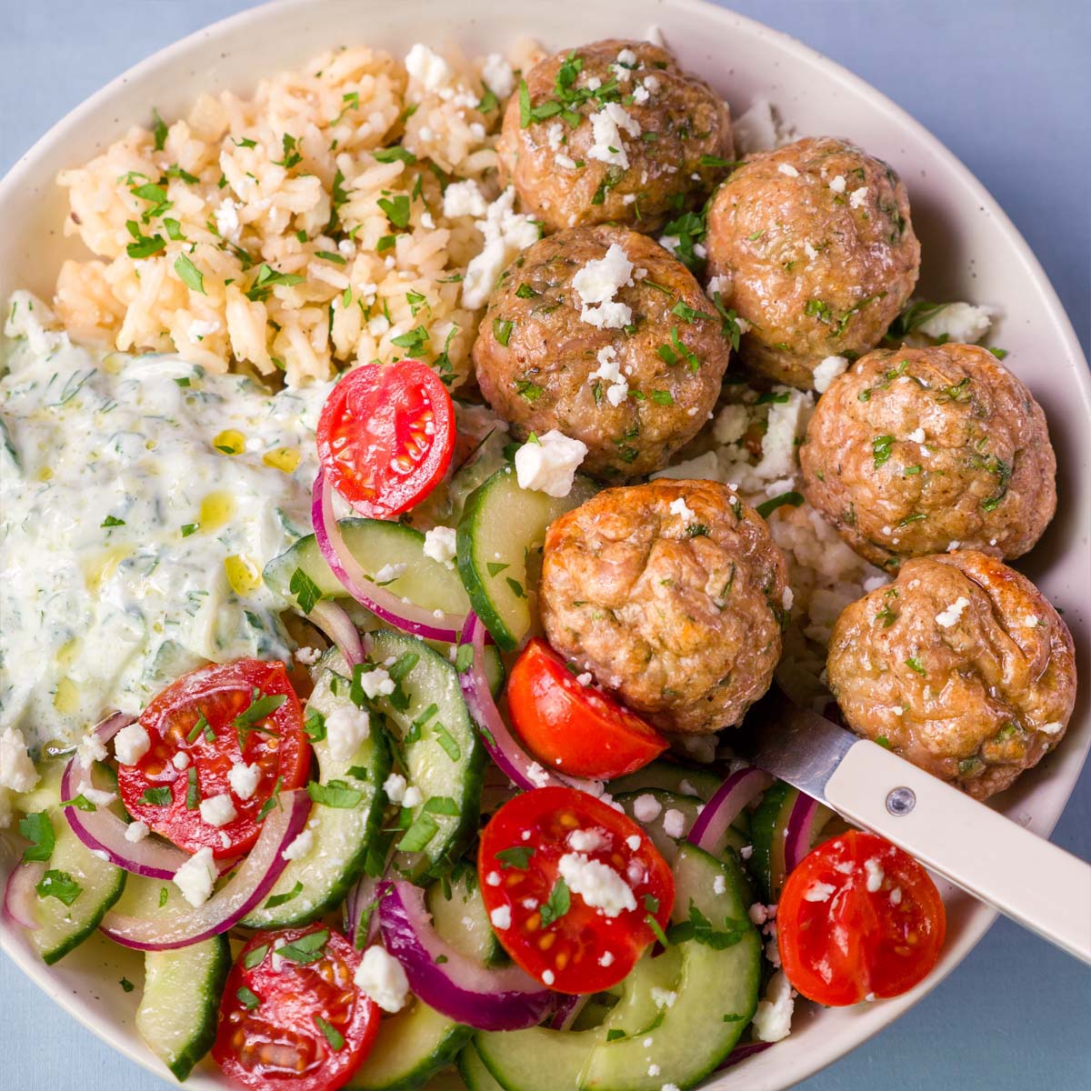 Mediterranean baked chicken meatballs with lemon rice, cucumber tomato salad, feta, and creamy tzatziki in a bowl