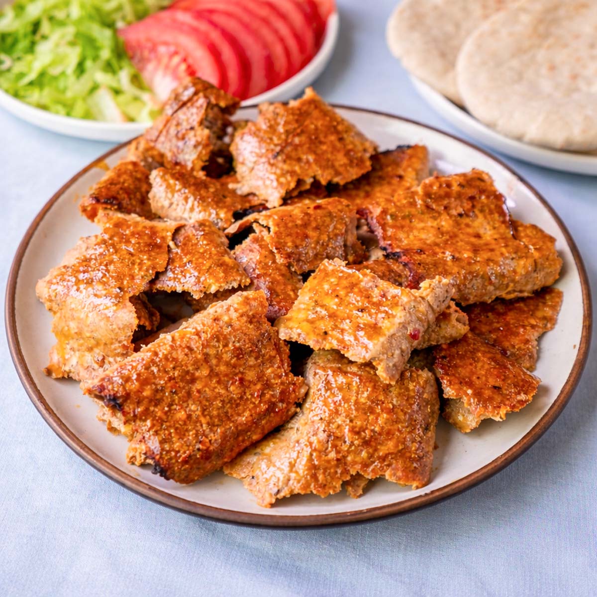 Viral doner kebab meat pieces on a plate with pita bread and sliced tomato in the background